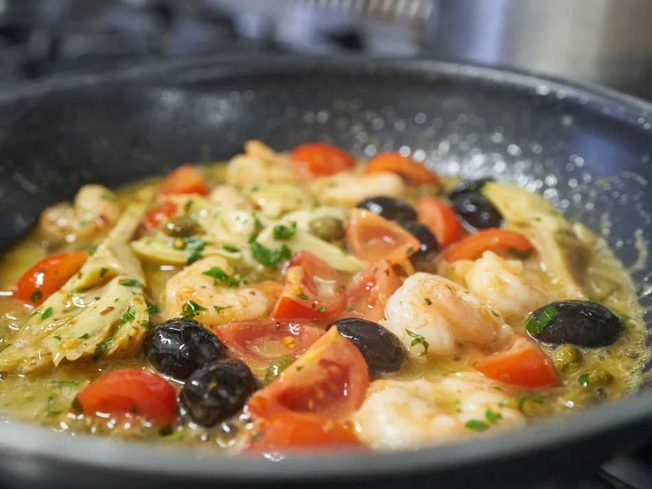 <think> Got it, let's create the alt text. The image shows a pan with seafood and vegetables—shrimp, tomatoes, olives, artic…