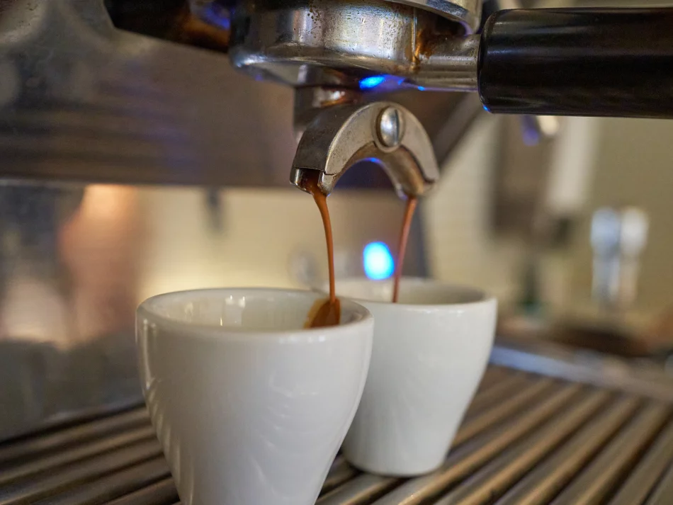 <think> Got it, let's create the alt text. The image shows an espresso machine pouring coffee into two white cups. Need to b…