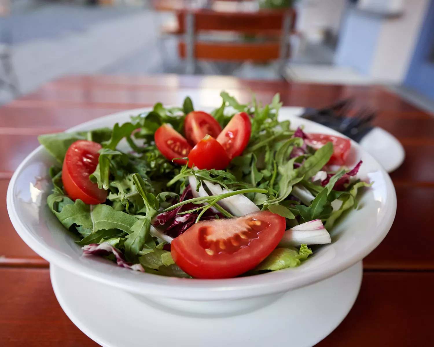 <think> Got it, let's create the alt text. The image shows a salad with arugula, tomato slices, and other greens on a white…